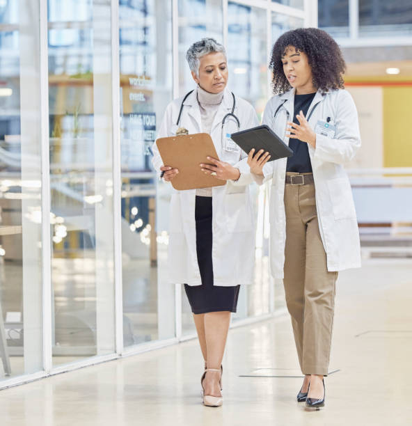 Collaboration, tablet and documents with woman doctors walking in a hospital for healthcare or medical discussion. Teamwork, medical and consulting with medicine professionals talking in a clinic